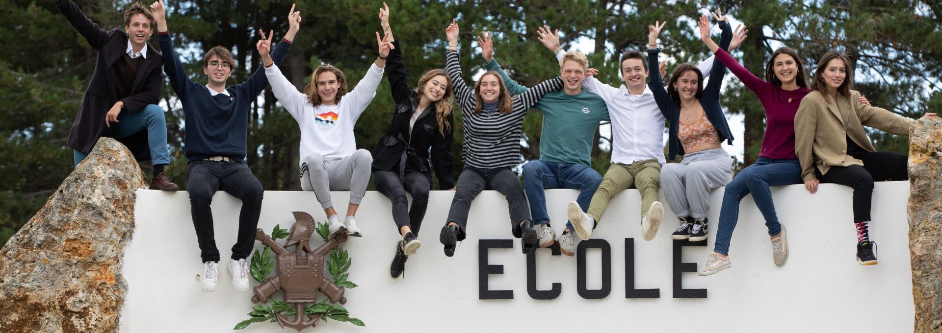 Students sitting on the Ecole Polytechnique sign, all cheering.